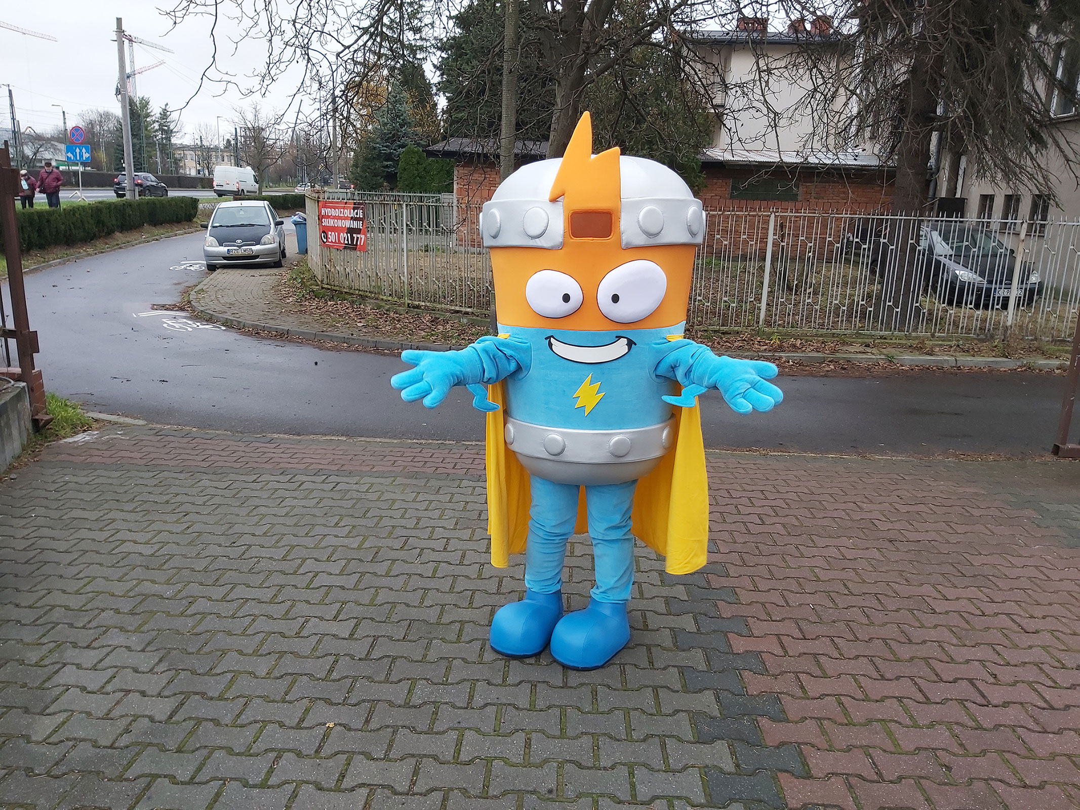 Na fotografii widnieje strój reklamowy Kid Kazoom SuperZings pozujący do zdjęcia przed siedzibą firmy Elabika stroje reklamowe